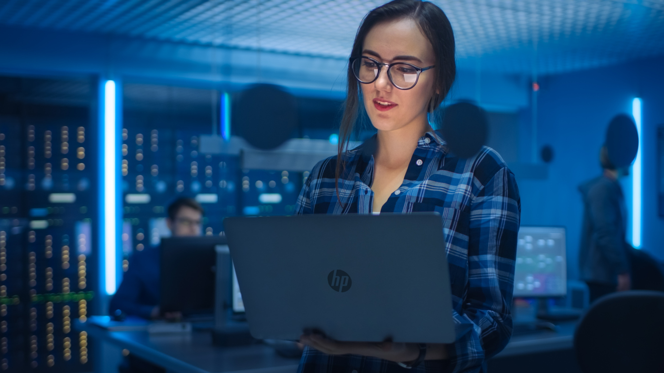 mulher segurando notebook em meio a data center representando as vantagens do windows 11 pro